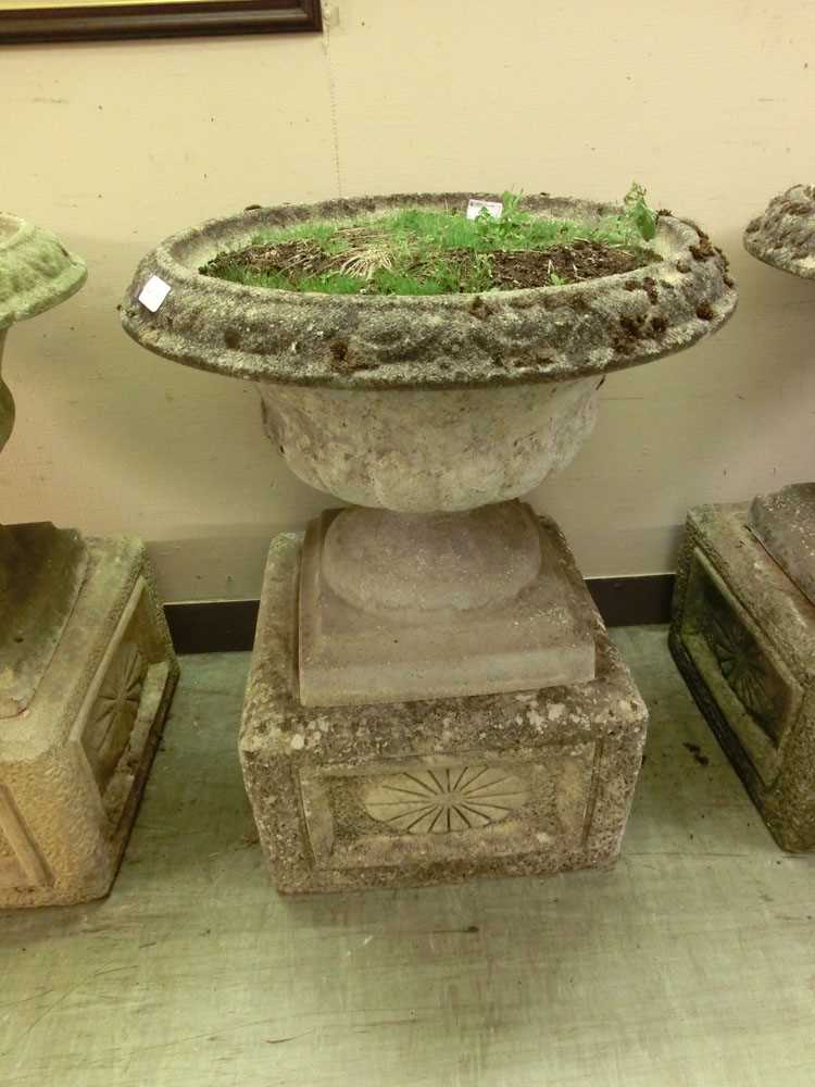 A composite stone garden urn on square floral decorated plinth