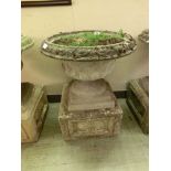 A composite stone garden urn on square floral decorated plinth