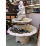 A composite stone garden water fountain modelled after boy holding shell over two tiers