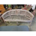 A weathered teak curved garden bench