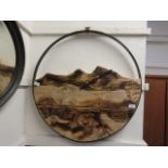 A modern circular metal clock having a scorched wooden mountain scene design