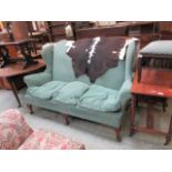 An early 20th century walnut framed humped back three seater settee upholstered in a green draylon