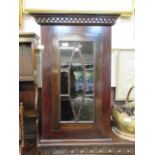 An early 20th century stained mahogany wall mounted glazed corner cupboard