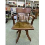 An early 20th century oak office chair with slatted back on swivel four leg base