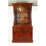 A reproduction Victorian style mahogany bookcase, the cornice over two glazed doors enclosing