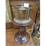 A brass and copper bottle holder on mahogany pedestal