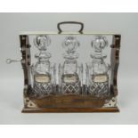 TANTALUS, silver-plated with three cut glass decanters and labels for whiskey, brandy and sherry,