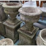 ARCHITECTURAL GARDEN URNS, on stands, a set of two, composite stone, grape detail on one pedestal