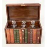 TANTALUS, early 20th century figured walnut and faux book spine with three glass decanters,