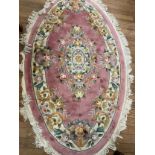 An oval rug with pink ground and a floral design, 230cm long and 130cm wide. A similar circular rug,