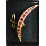 A 9ct gold crescent shaped brooch set with red stones.