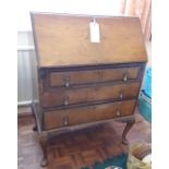 A walnut bureau with a writing desk over three drawers