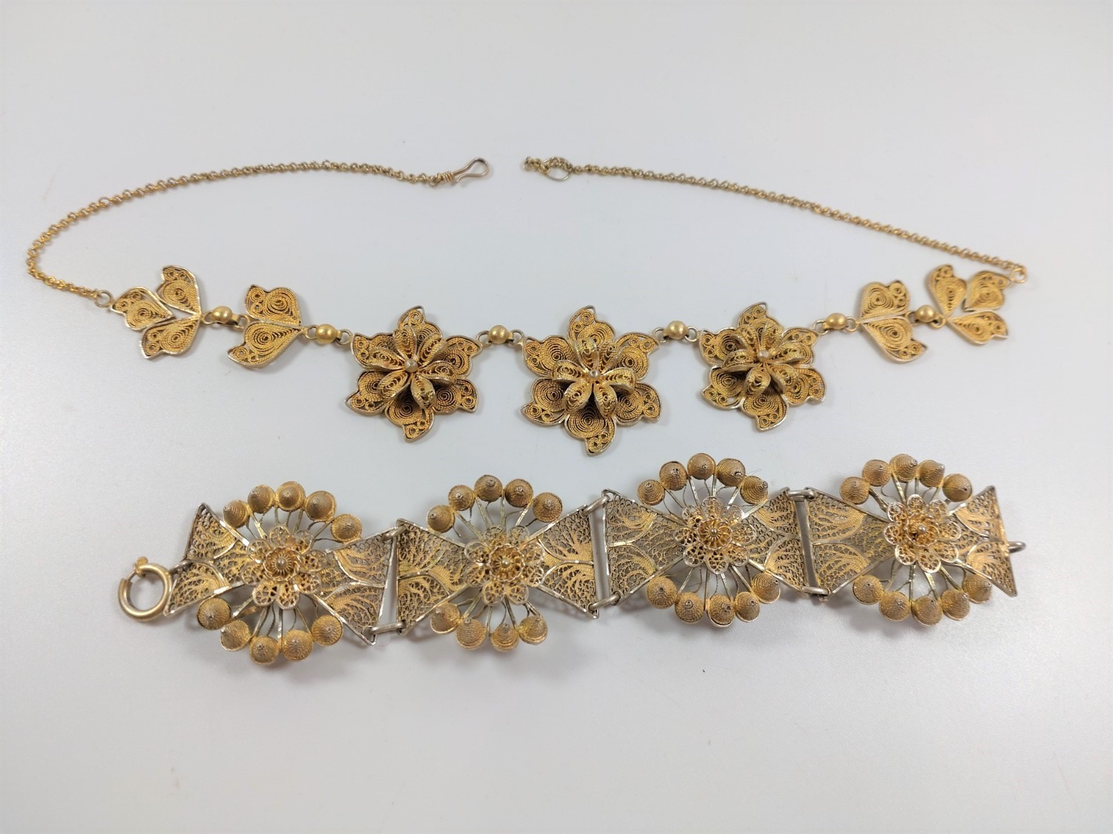 A gold colour metal bracelet and a gold colour metal necklace, each plaque in the form of a flower