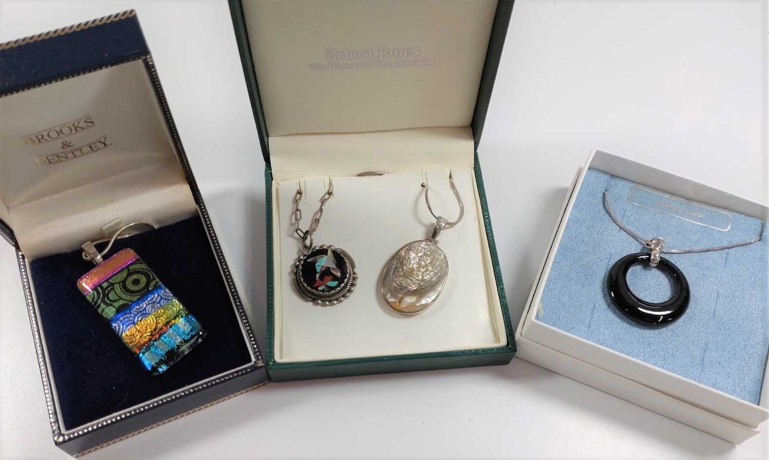 A collection of four silver necklaces with various decorative pendants, all boxed.