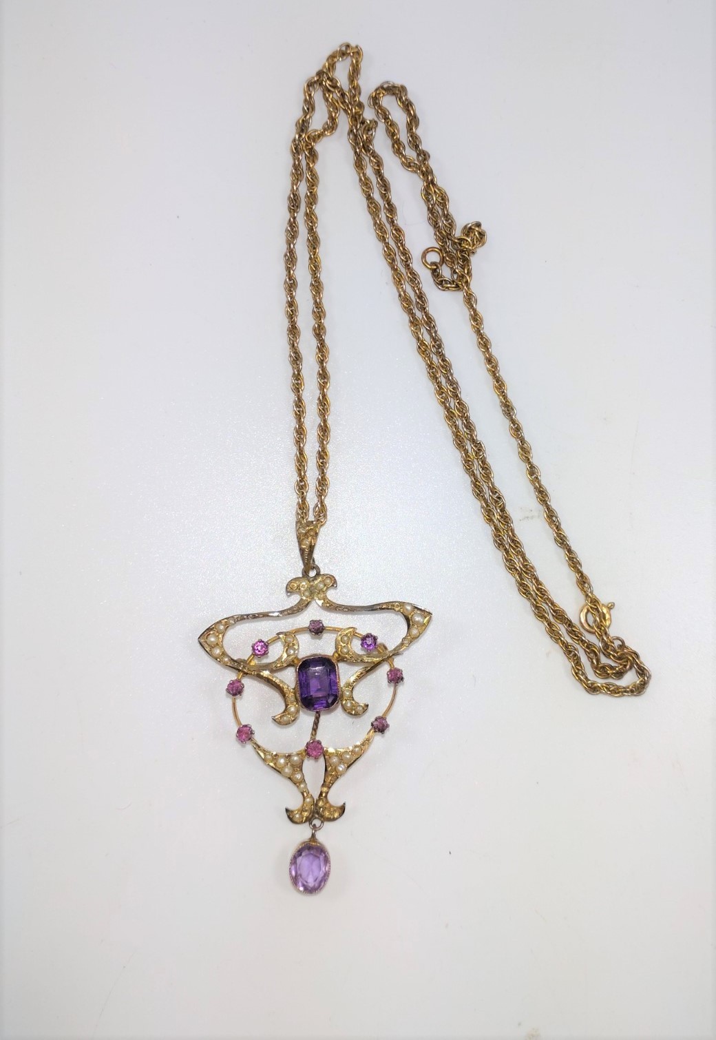 An Art Nouveau pendant set with amethyst and pearls in a gold colour metal frame on a long neck