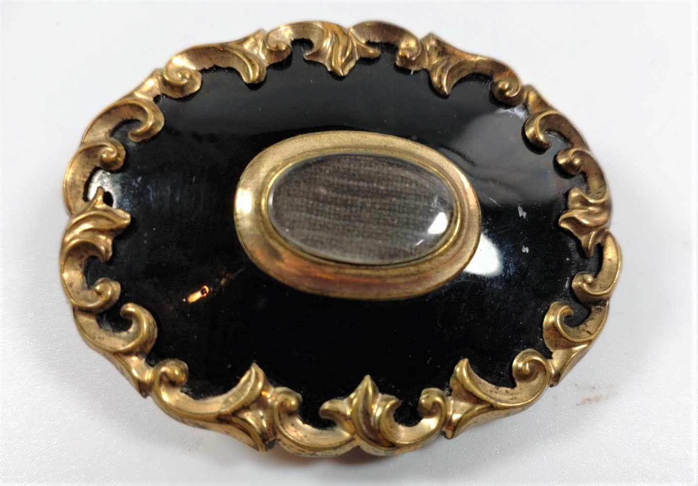 A Victorian Memorial brooch in black enamel and gold colour metal, with a framed lock of hair to