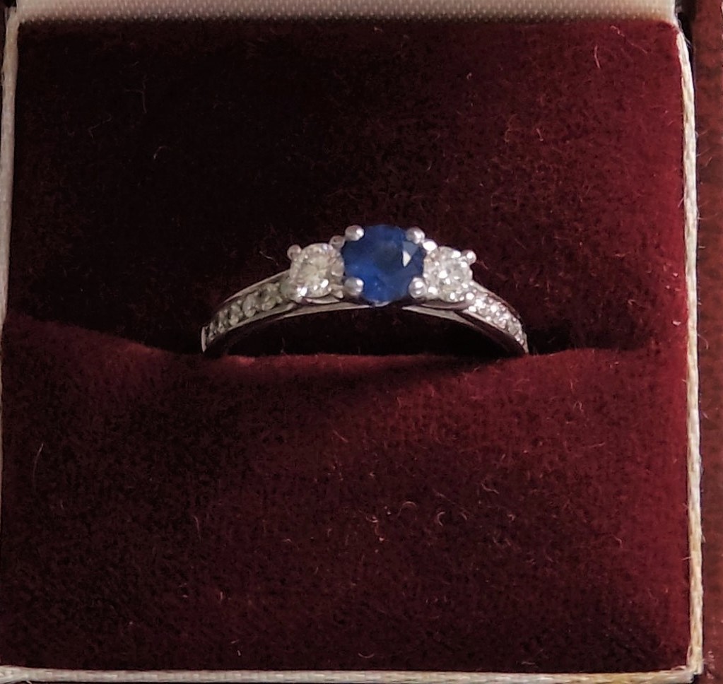 A white colour metal ring set with 55-point centre sapphire and 6-side diamond, two larger diamond