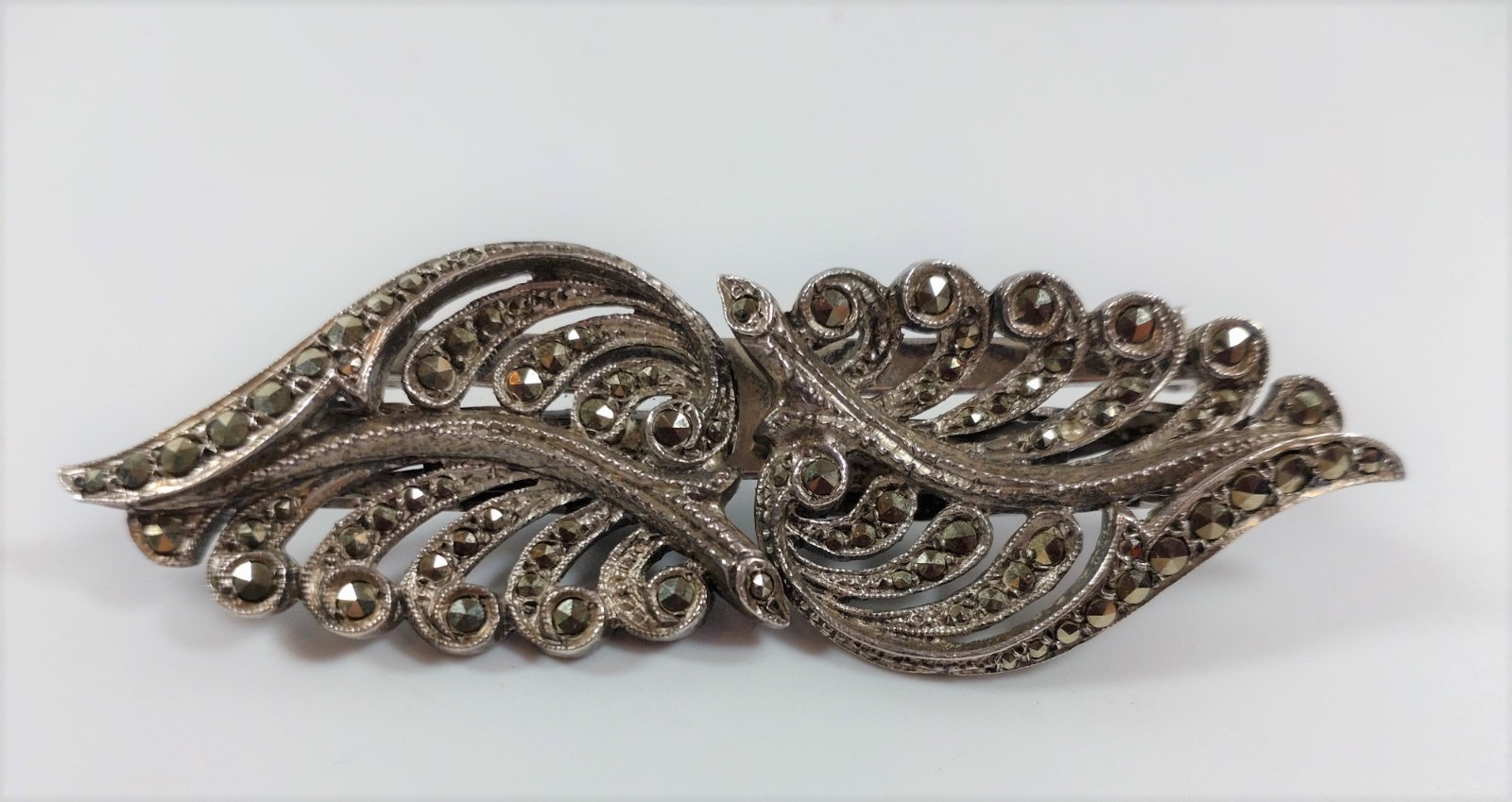 A Marcasite double clip in white metal together with an arts and crafts plaque in white metal.