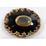 A Victorian Memorial brooch in black enamel and gold coloured metal, with a framed lock of hair to