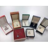A collection of eight silver necklaces, all with boxes, and various designs.