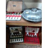 A collection of boxed cutlery, a plated vegetable dish and cover.