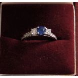 A white colour metal ring set with 55-point centre sapphire and 6-side diamond, two larger diamond