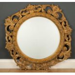 A circular wall mirror with a painted carved scrolling frame and bevelled glass, 78cm wide x 89cm