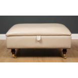A cream leatherette upholstered footstool with lift top, on turned supports and casters, 88cm wide x