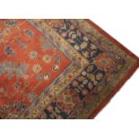 An old Turkey Oushak carpet with repeating stylistic flower design on a rust red ground, holed and