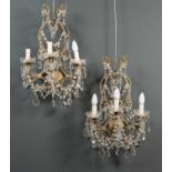 A pair of gilt metal and cut glass three branch wall lights on scrolling metal frames with strings