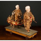 A Victorian pull along toy formed as three china headed dolls, one pulling a small cart with the