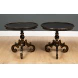 A pair of ebonised and gilt decorated lamp tables with circular dish tops on scrolling feet with