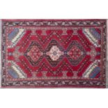 A late 20th century Middle Eastern red ground rug with three stepped diamond motifs and a banded