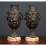 A pair of metal urns on marble bases, the urns with lion mask and foliate decoration, on stepped