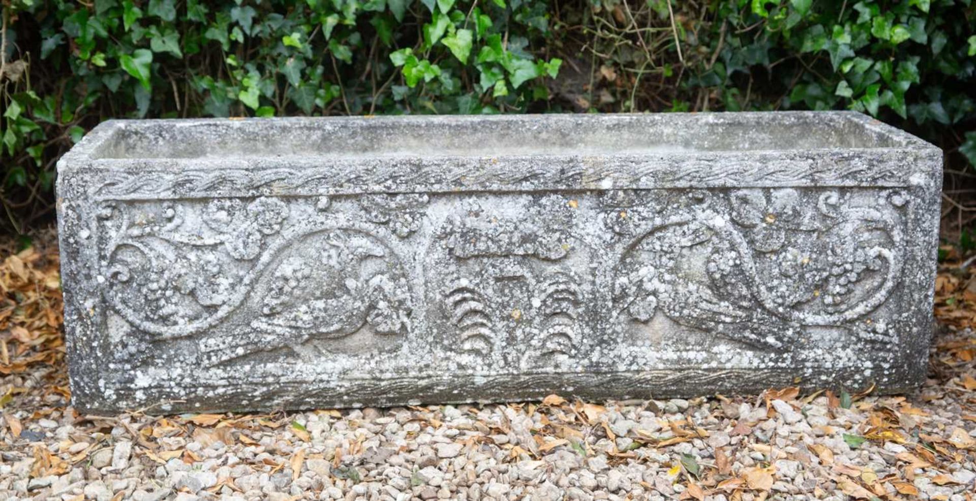 A cast reconstituted stone trough with fruiting vine and peacock ornament, 120cm wide x 38.5cm