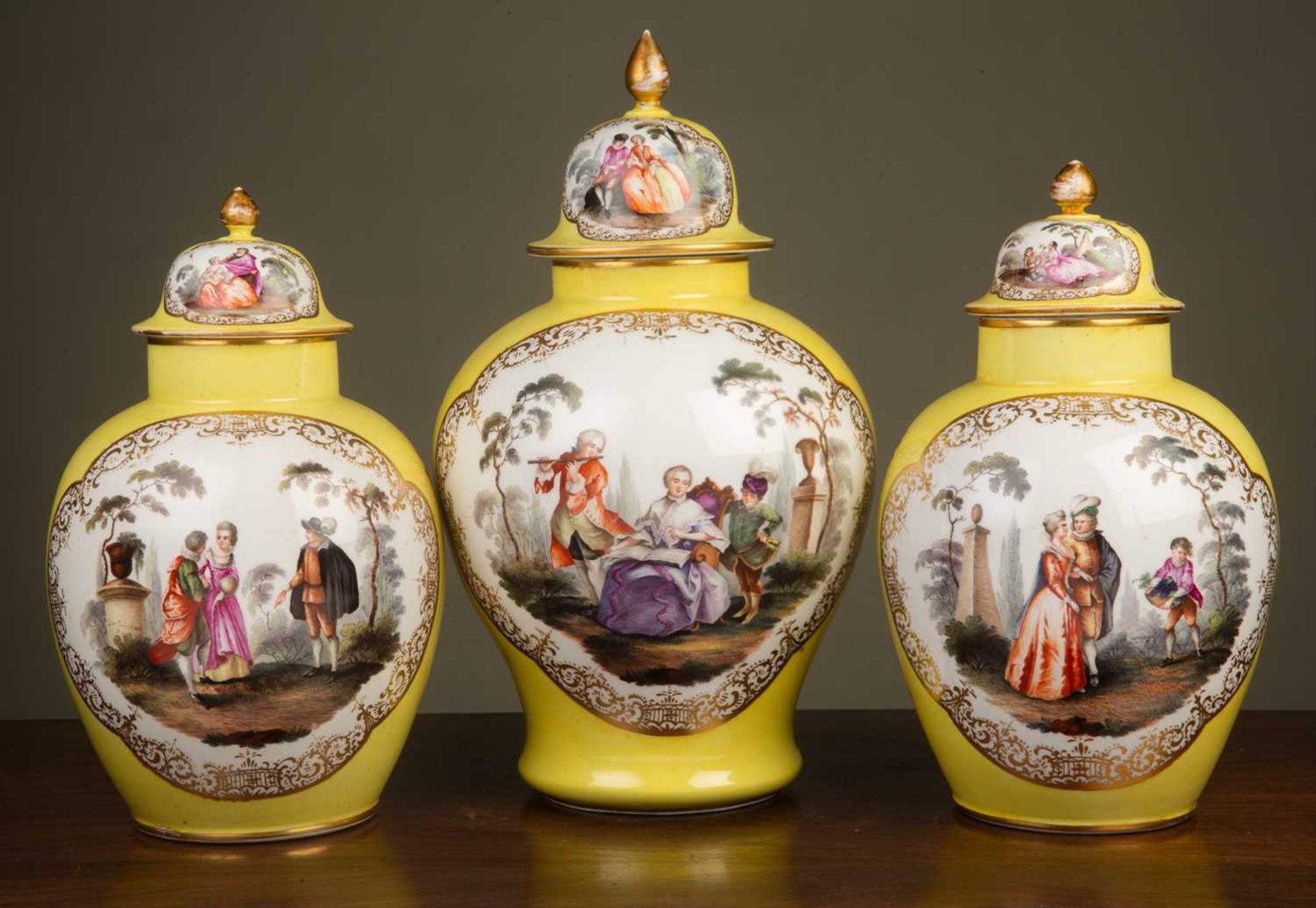 A garniture of three Dresden yellow ground ovoid vases and covers decorated to one side with