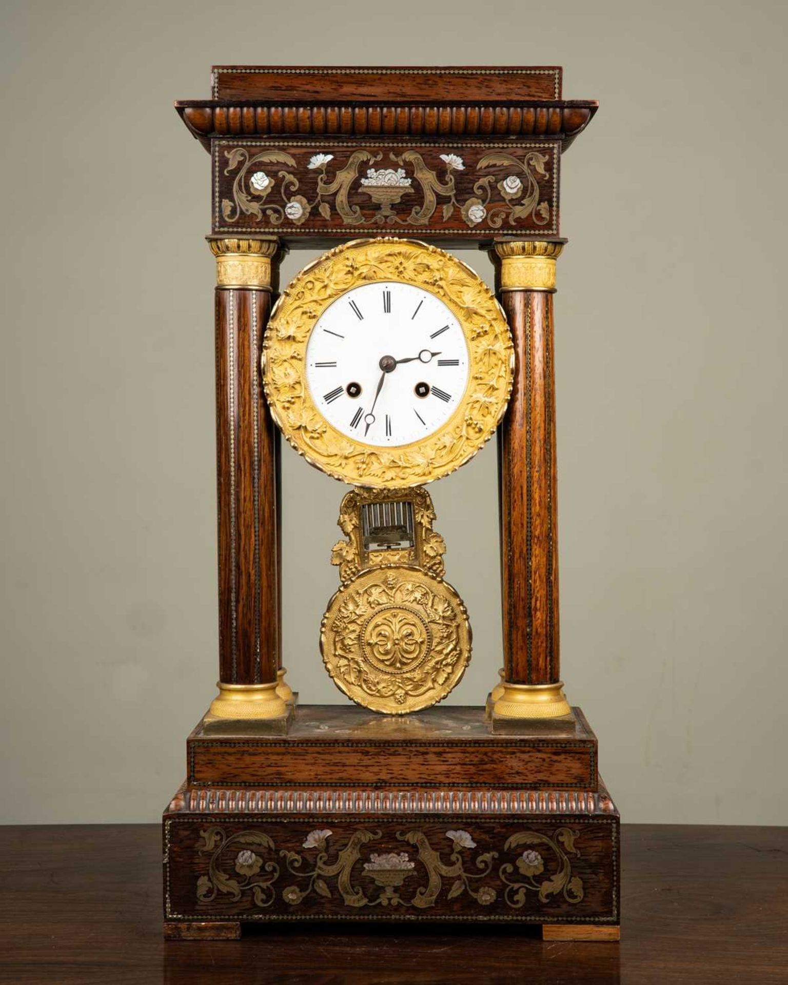 A French walnut portico clock with brass and mother of pearl decoration, the white enamel dial