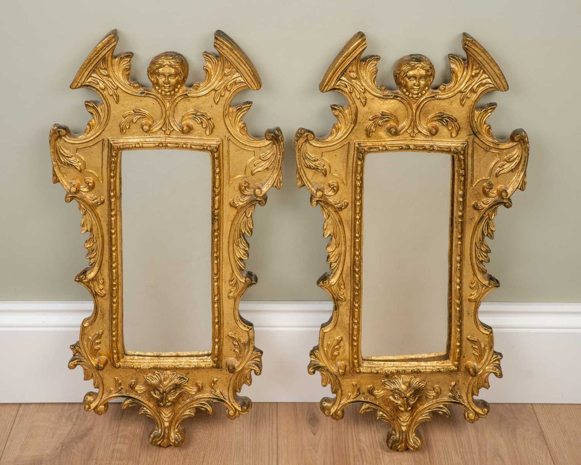 A pair of modern decorative gilt composite moulded wall mirrors with mask ornament to the break arch