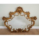 A decorative gilt wall mirror shaped mirror plate within a scroll carved frame, with floral swags,