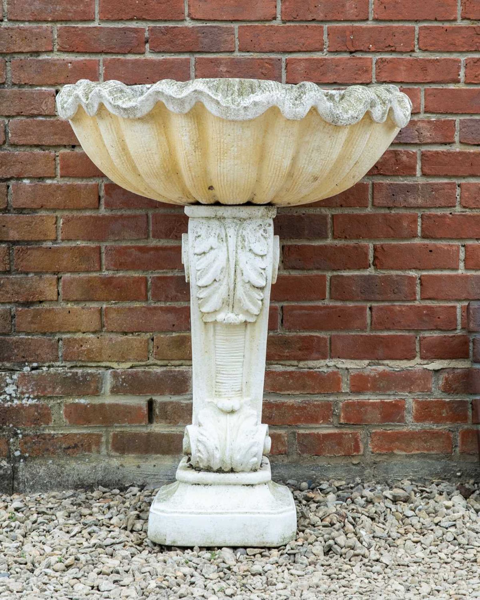 A cast reconstituted stone wall fountain in the form of a large shell on supporting pedestal with