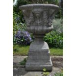 A cast reconstituted stone garden urn decorated with masks and fruiting swags, on fluted square