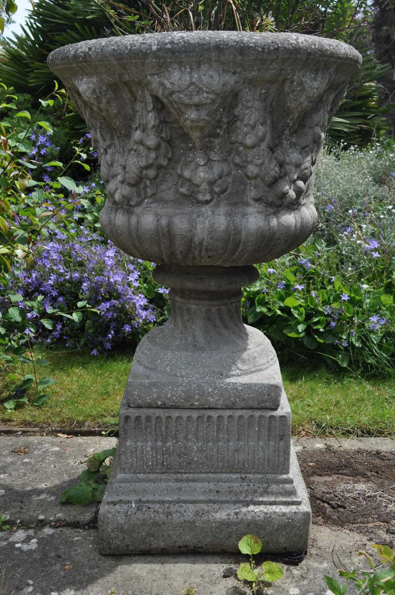 A cast reconstituted stone garden urn decorated with masks and fruiting swags, on fluted square