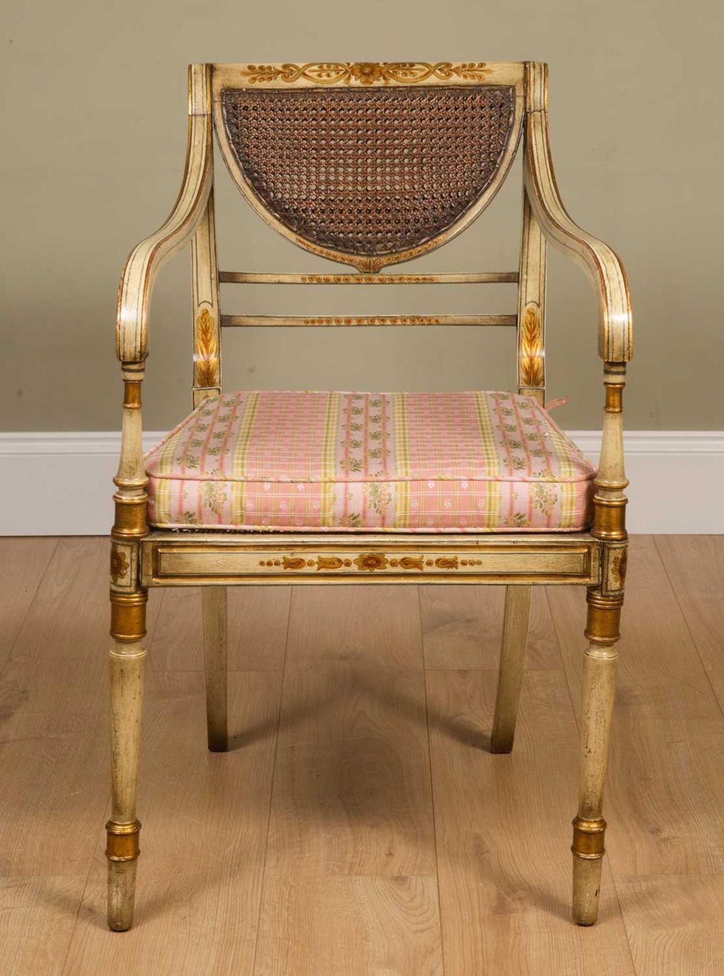 A Regency-style painted elbow chair, with caned back and seat, squab cushion, all standing on turned