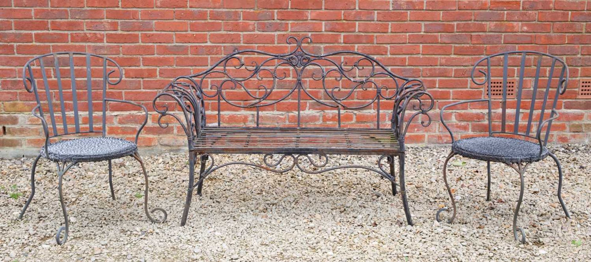 A black painted wrought iron garden seat, with scroll ornament to the back and arms, 141cm wide,