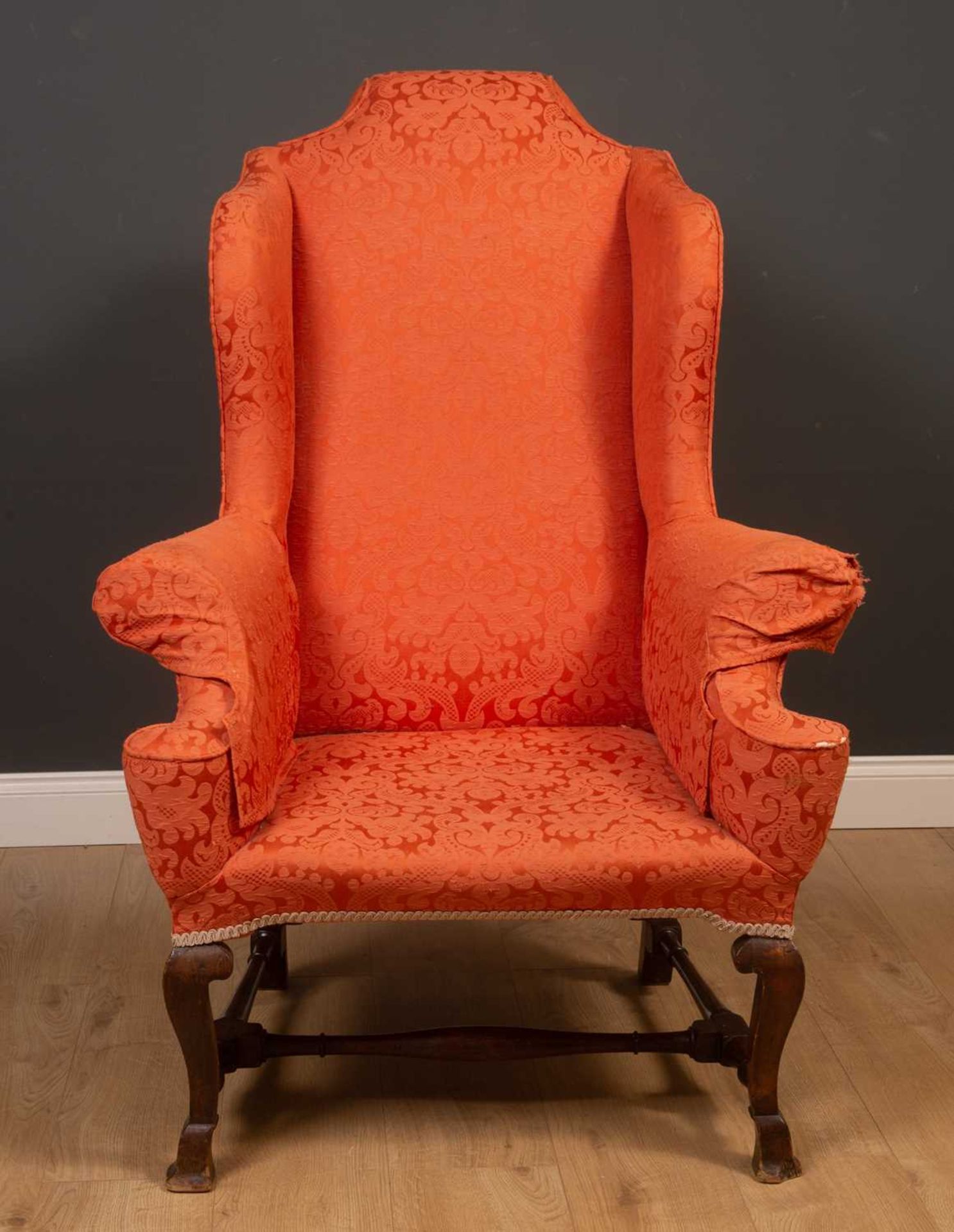 A Georgian mahogany high wingback armchair on scrolling supports united by an H-frame stretcher,