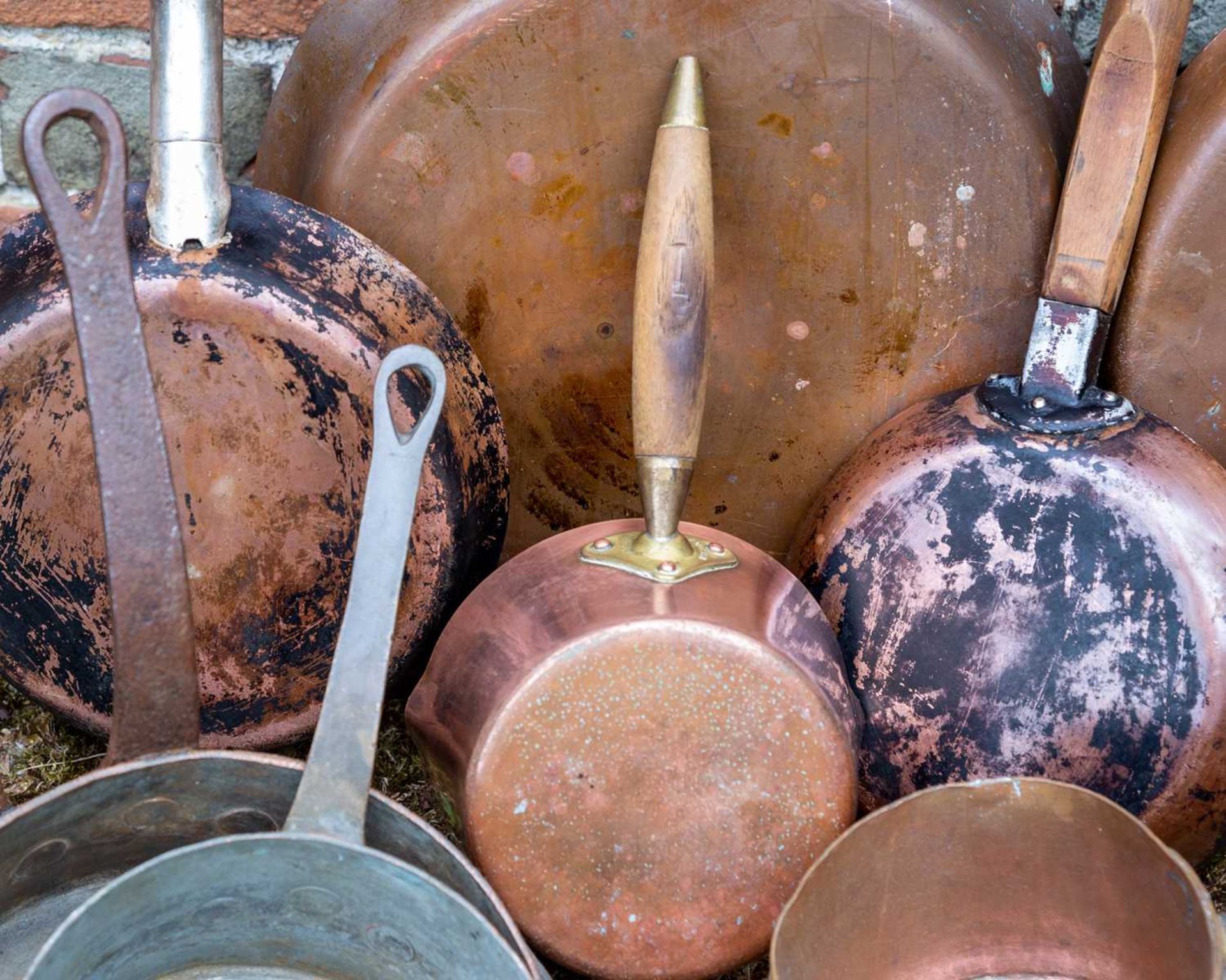 A group of copper saucepans, frying pans and further items, some with iron handles, some with wooden