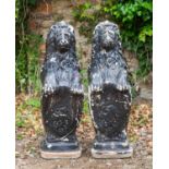 A pair of black painted cast reconstituted stone heraldic lions seated holding shields, each