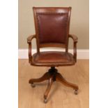 An oak framed desk chair with leather upholstered seat and seat back, on rotating tripod base and