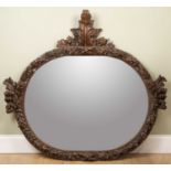 A carved oval wall mirror, decorated with acanthus leaves and fruiting branches, 139cm wide, 130cm