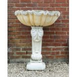 A cast reconstituted stone wall fountain in the form of a large shell on supporting pedestal with